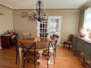 A dining room with a round wooden table, four chairs, a chandelier, and a view of the outside through a door. - The Gnome Home in McKennan Park (Sioux Falls)