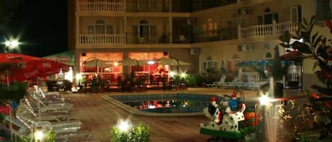 Un patio de hotel con mobiliario exterior, piscina y fuente.