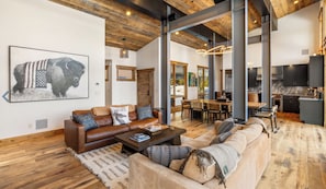 A spacious living area with a brown leather sofa, a beige sofa, and a coffee table. There is a large painting on the wall and a wooden ceiling. - Private Luxury Mountain Retreat 3 bdrm w hot tub—near Big Sky & Yellowstone (Big Sky)