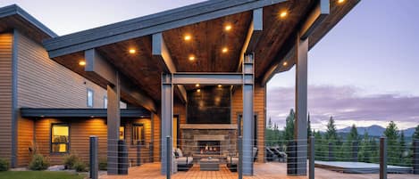 A modern house with a covered outdoor area featuring a fireplace and seating.