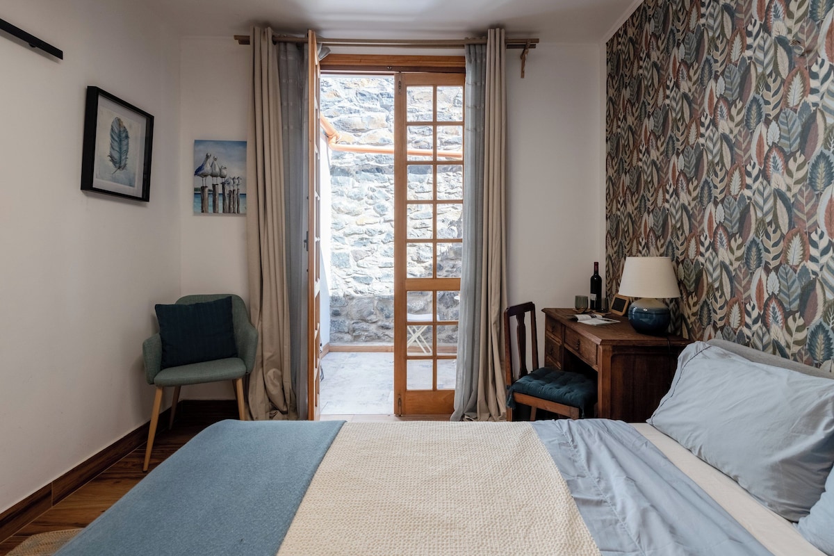 Un dormitorio con cama, una silla, un escritorio y vistas a través de una puerta.