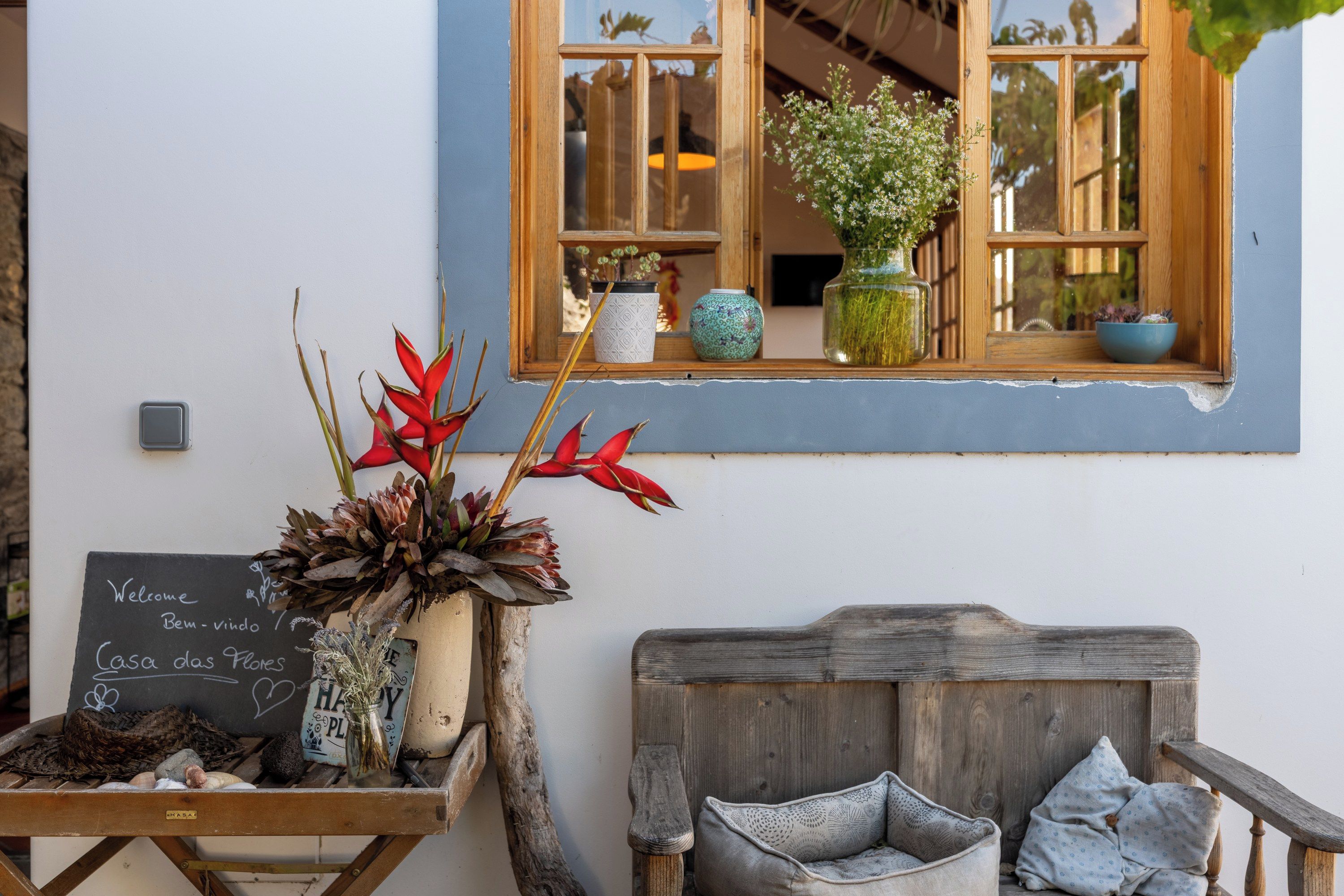 Un interior rústico con un letrero en pizarra, muebles de madera y una ventana con plantas.