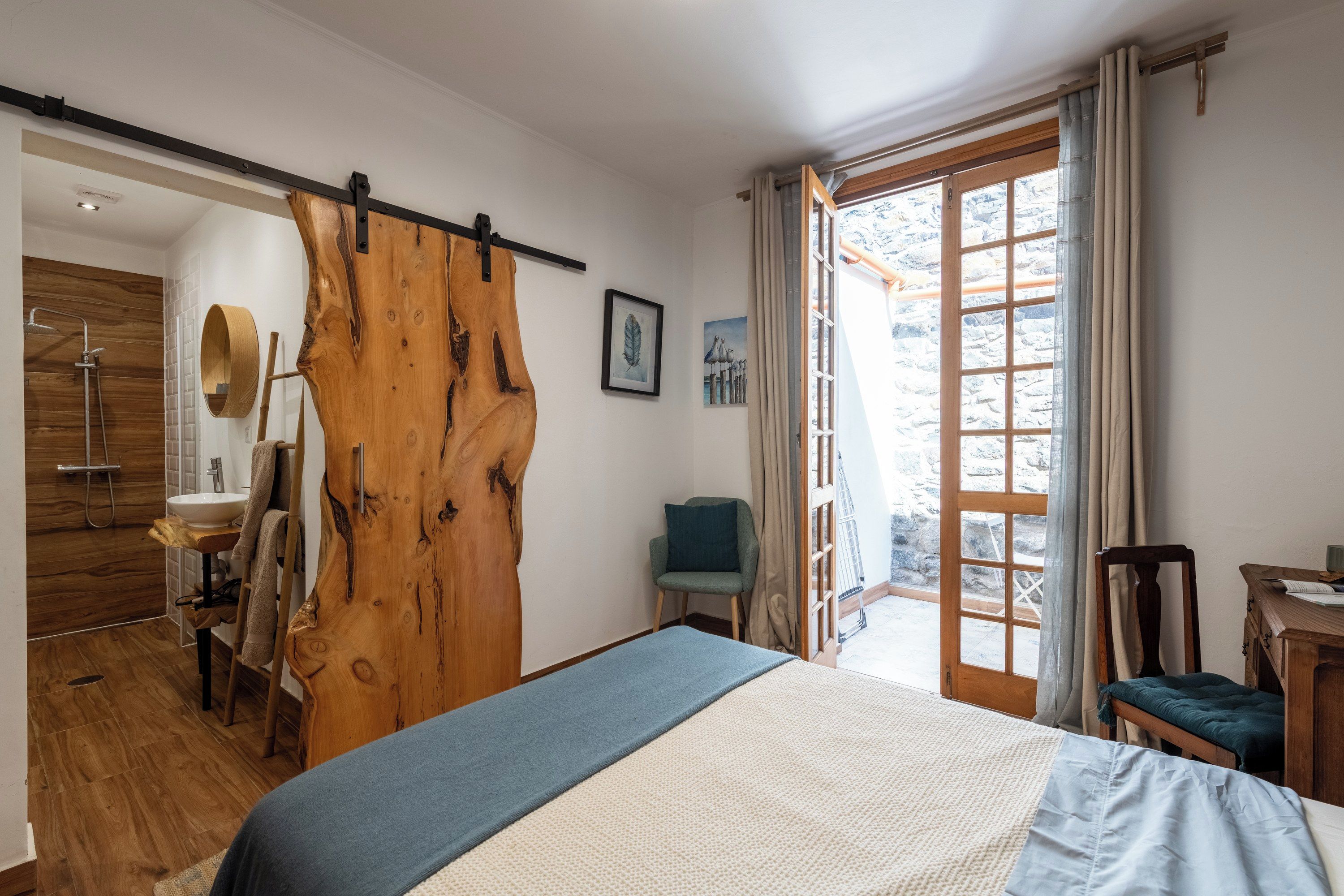 Un dormitorio con una puerta de madera grande, una cama, una silla, un escritorio y vistas al exterior.