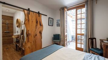 Un dormitorio con una puerta de madera grande, una cama, una silla, un escritorio y vistas al exterior.
