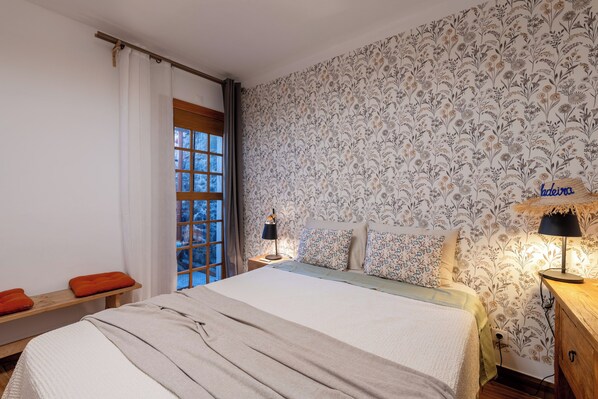 A bedroom with a bed, a nightstand, a lamp, and a window with curtains.