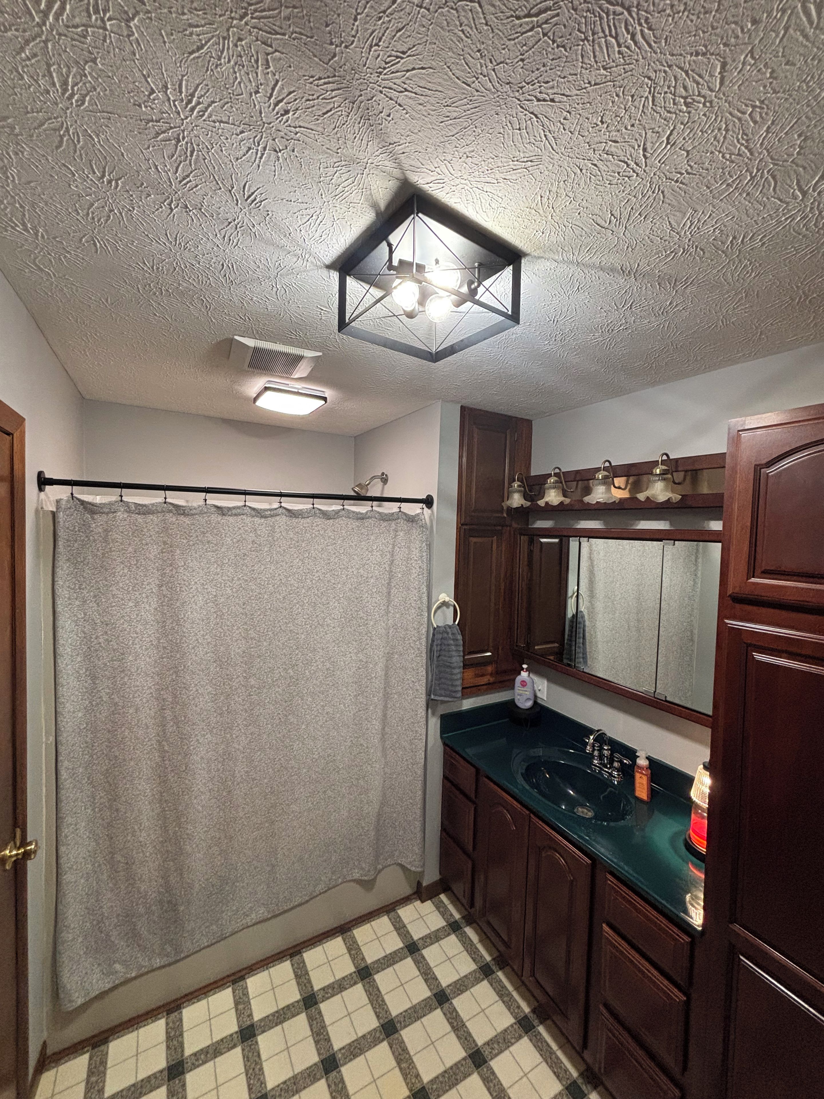 A bathroom with a shower curtain, a sink, a mirror, and a ceiling light fixture.
