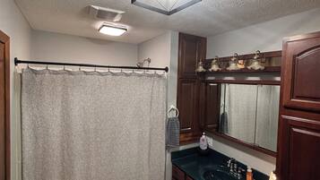A bathroom with a shower curtain, a sink, a mirror, and a ceiling light fixture.