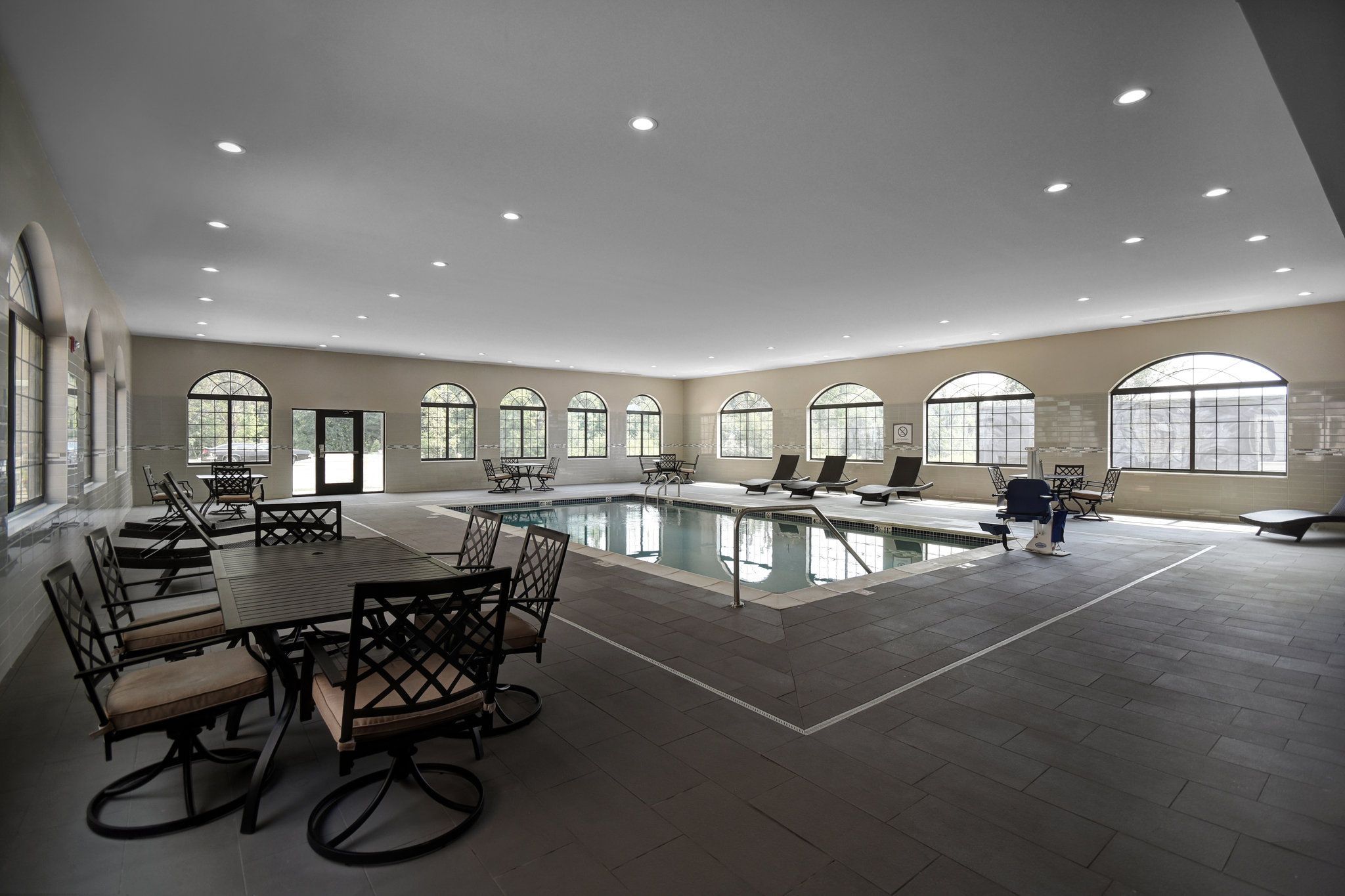 Un vaste espace abritant une piscine intérieure, doté de nombreux coins salon et de grandes fenêtres.