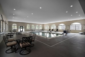 Un vaste espace abritant une piscine intérieure, doté de nombreux coins salon et de grandes fenêtres.