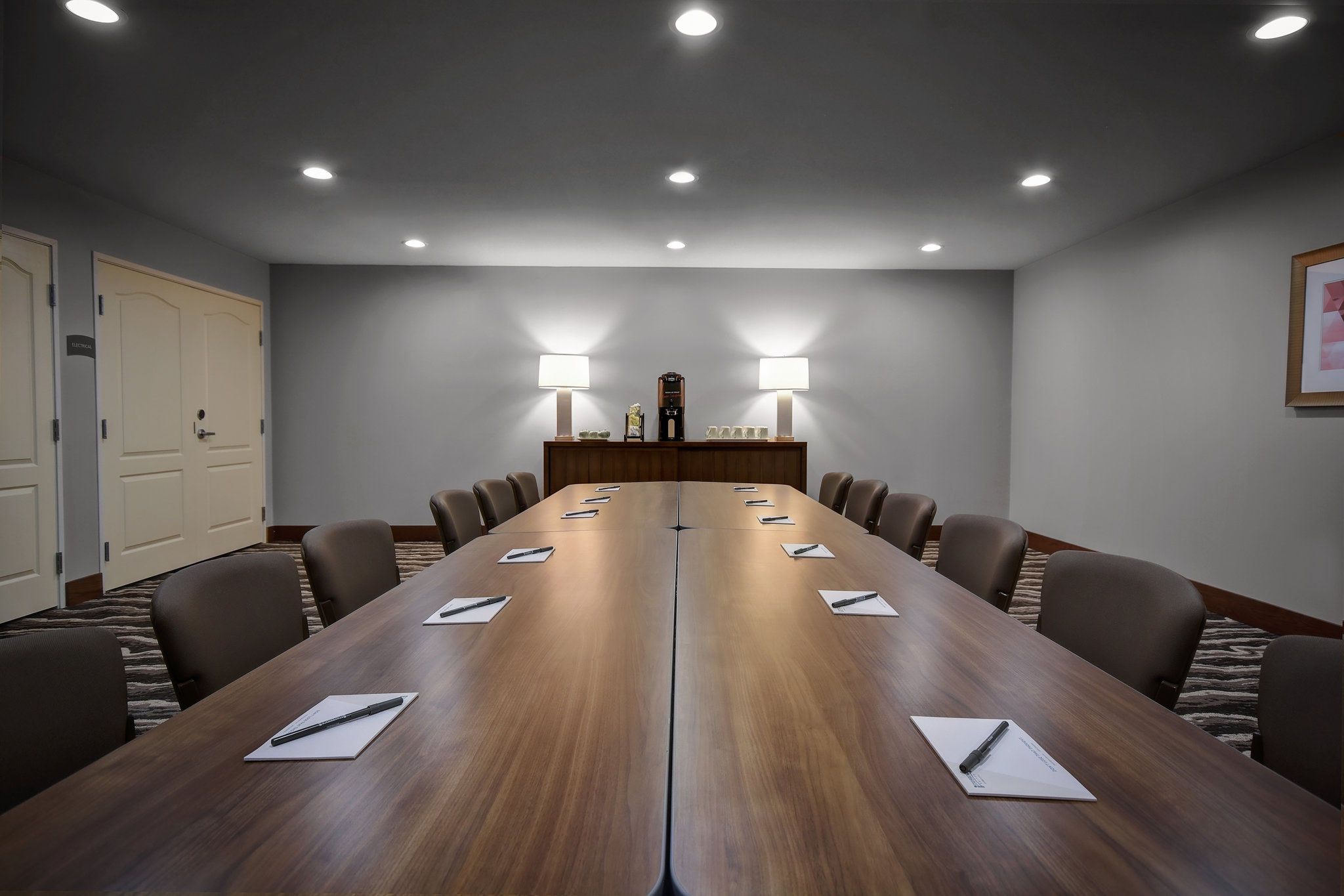 A conference room with a long table, chairs, and two wall-mounted lamps.