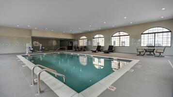 Une piscine intérieure avec des parois en verre transparent, un sol carrelé et quelques chaises longues.