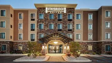 Un hôtel Staybridge Suites doté d’une façade en pierre, de nombreuses fenêtres et d’une entrée bien éclairée.