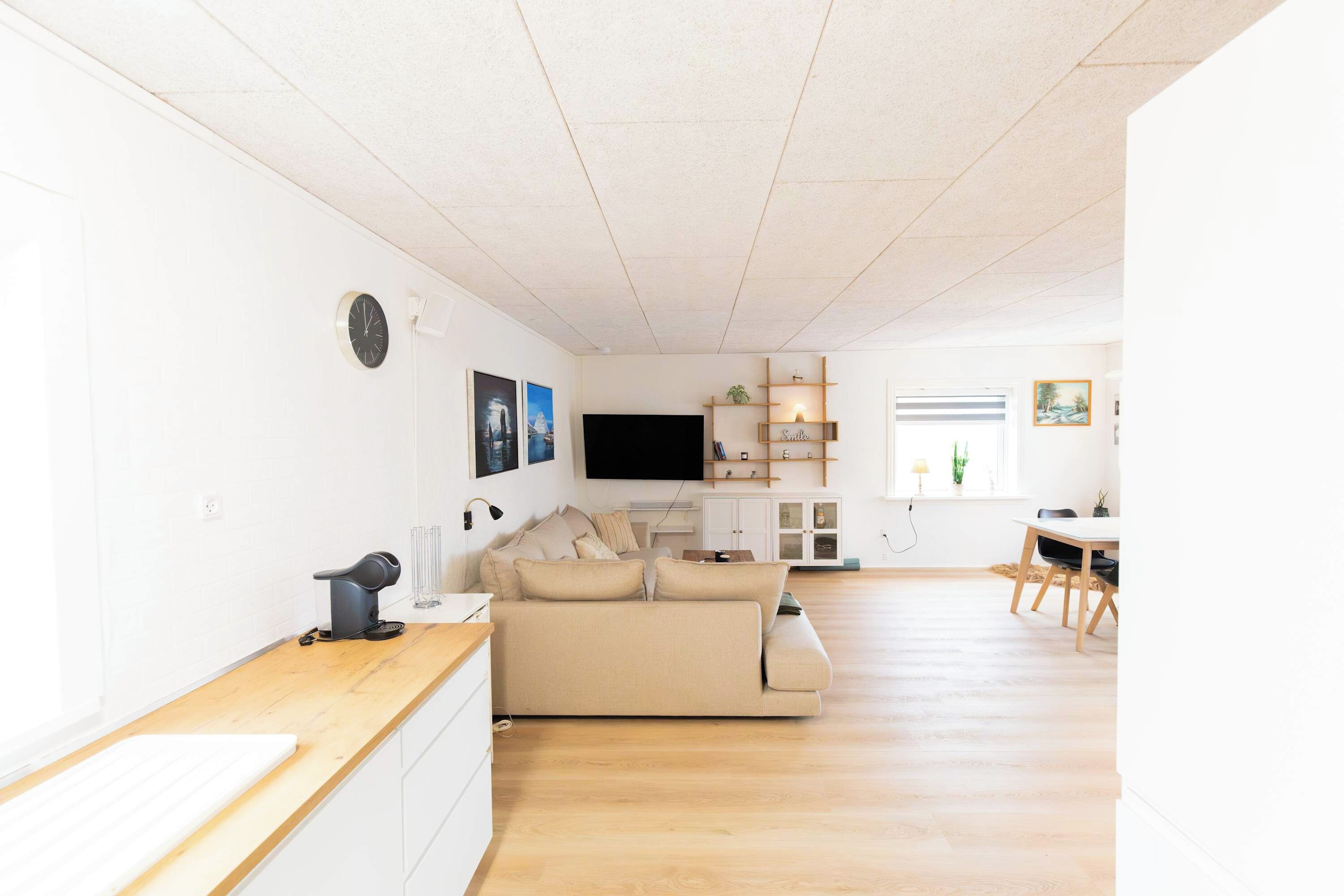 A modern living room with a sofa, a flat-screen TV, and a dining area with a table and chairs.