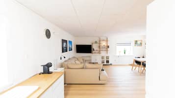 A modern living room with a sofa, a flat-screen TV, and a dining area with a table and chairs.