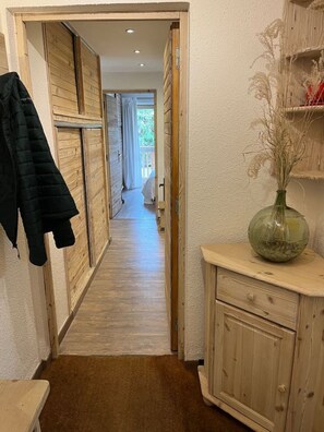 Un pasillo con puertas de madera, un perchero, un jarrón con plantas secas y un armario de madera.