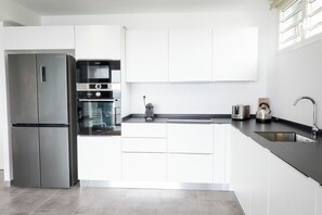 A modern kitchen with stainless steel appliances, white cabinetry, and a black countertop. - Ti Soleil: Exceptional Ocean View (Les Anses-d'Arlet)