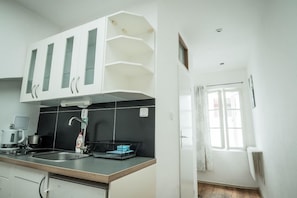 A kitchen with white cabinets, a black backsplash, a sink, and a window with curtains. - Charles Bridge Hostel & Apartments (Prague)