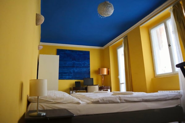 A hotel room with a bed, a desk, a lamp, a television, and a large window. - Charles Bridge Hostel & Apartments (Prague)