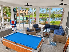 A pool table in a sunlit room with wicker furniture and a view of a pool and palm trees. - Paddle Point | Weeki Wachee Main River & Kayaks (Weeki Wachee)