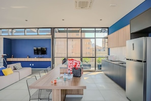 A modern kitchen with a large refrigerator, a dining area with a table and chairs, and a blue accent wall. - Studio Metr Santa Cec lia Piscina e Rooftop (São Paulo)
