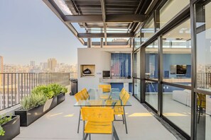 A modern balcony with a glass table and chairs, a city view, and a small seating area with cushions. - Studio Metr Santa Cec lia Piscina e Rooftop (São Paulo)