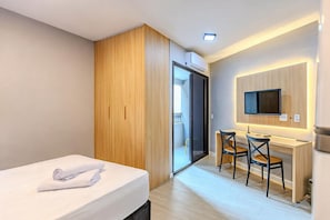 A hotel room with a bed, a desk with two chairs, a TV mounted on the wall, and a wardrobe. - Studio Metr Santa Cec lia Piscina e Rooftop (São Paulo)