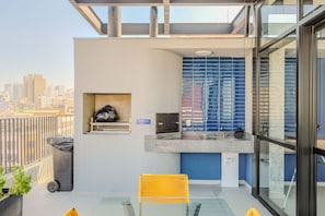 A modern balcony with a glass table, a yellow chair, a trash bin, and a small shelf with a bag. - Studio Metr Santa Cec lia Piscina e Rooftop (São Paulo)