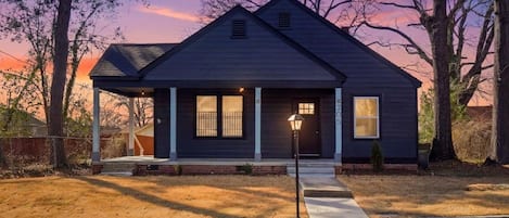 A two-story house with a dark exterior, a covered porch, and a well-lit front door.