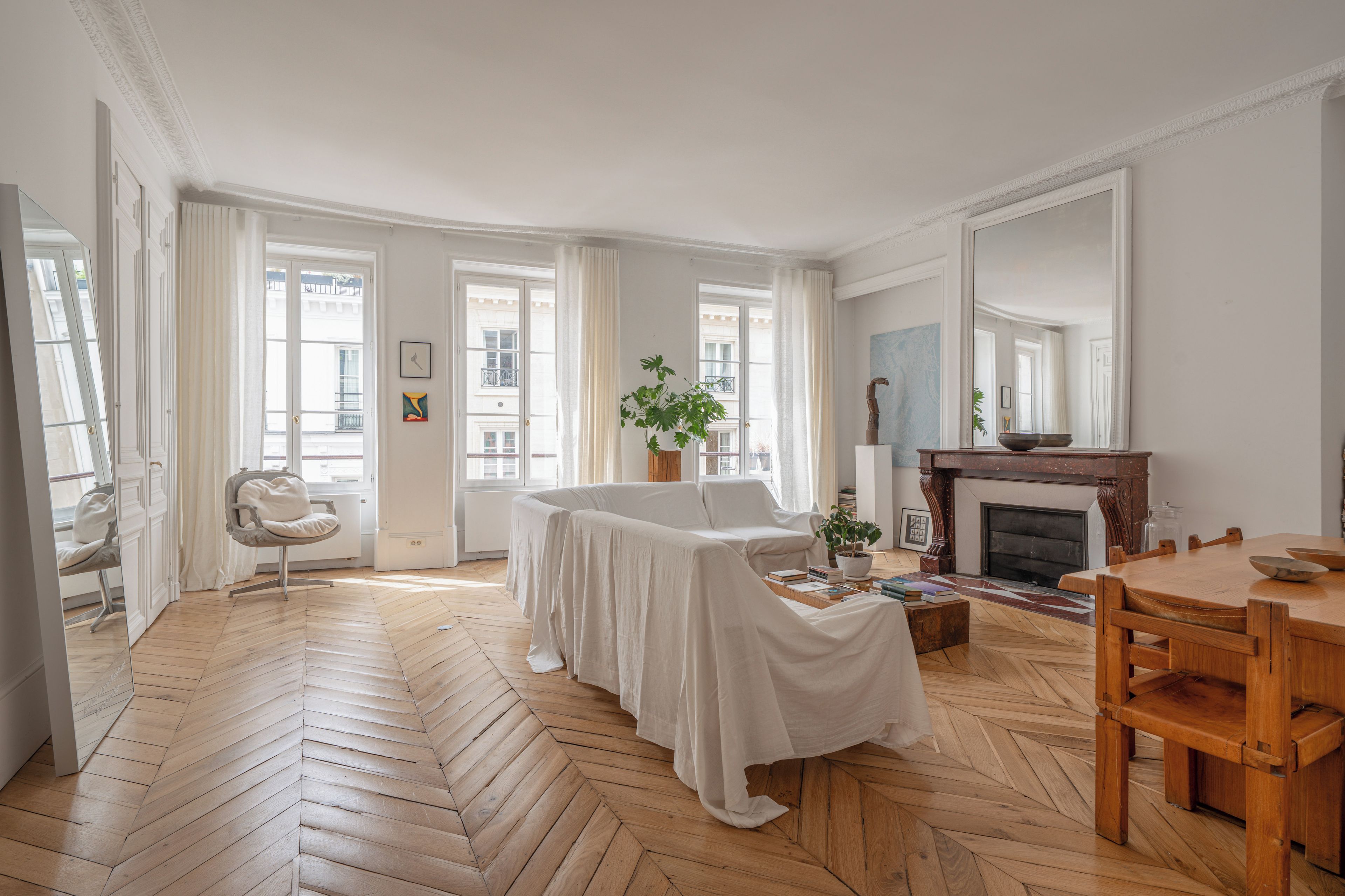 A spacious room with a herringbone floor, a fireplace, a dining table with chairs, and a large mirror.