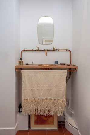Ein Badezimmer mit einem Holzwaschtisch, einem Spiegel, einem Handtuch und einer Kupferleitung.