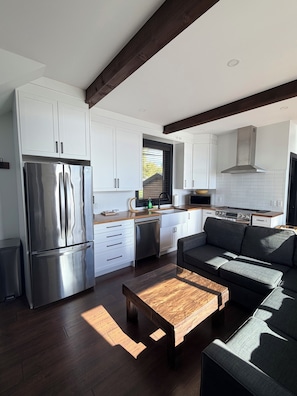 A modern kitchen with white cabinets, stainless steel appliances, and a wooden dining table. - Camp Canakiwi (Shuniah)