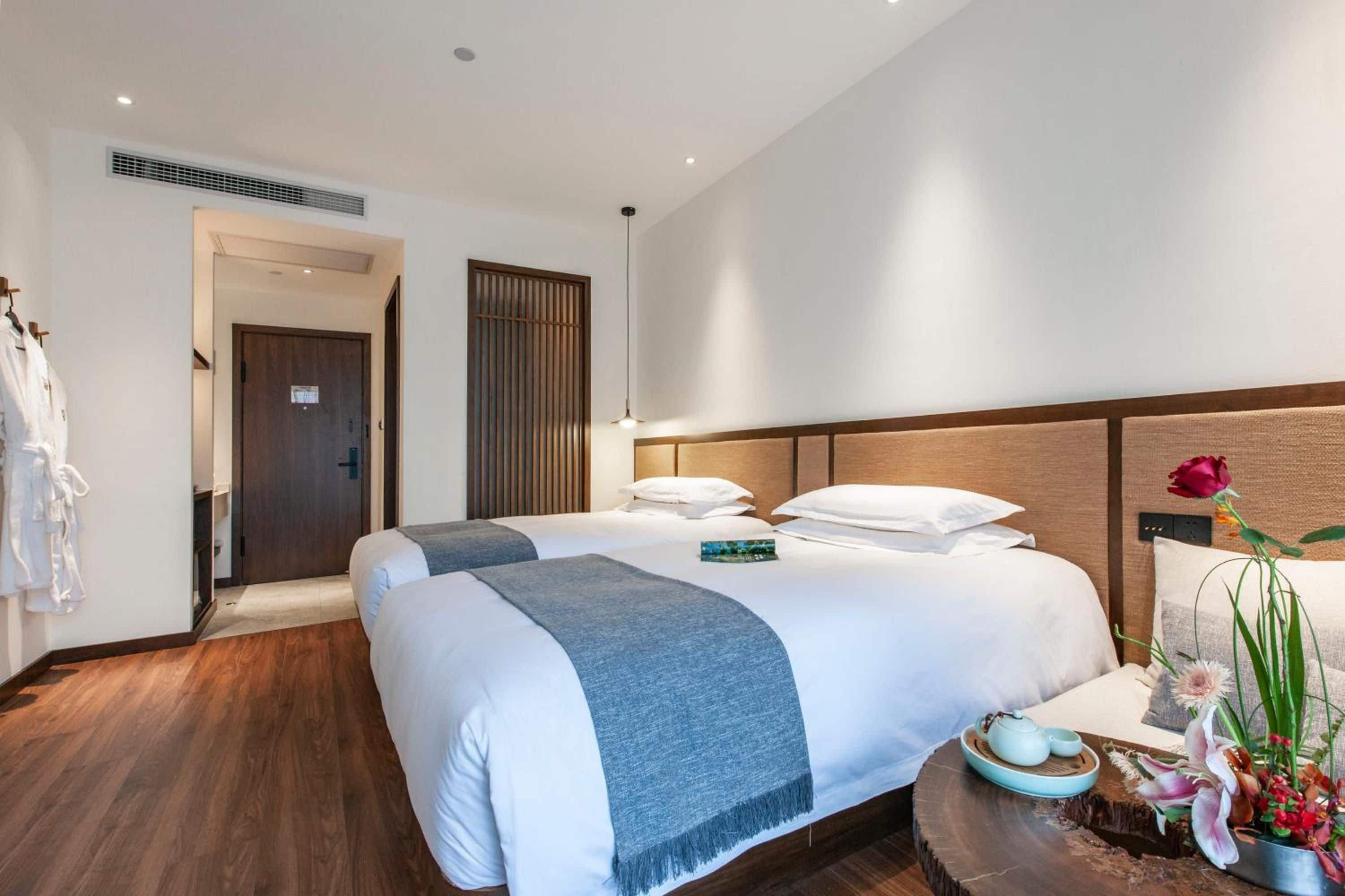 A hotel room with a large bed, a bedside table with a vase of flowers, and a wooden headboard.