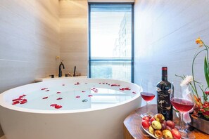 A modern bathroom with a freestanding bathtub, a window with blinds, and a table with a bottle of wine, glasses, and fruit. - Ssaw Boutique Hotel Hangzhou Liangyun (Hangzhou)