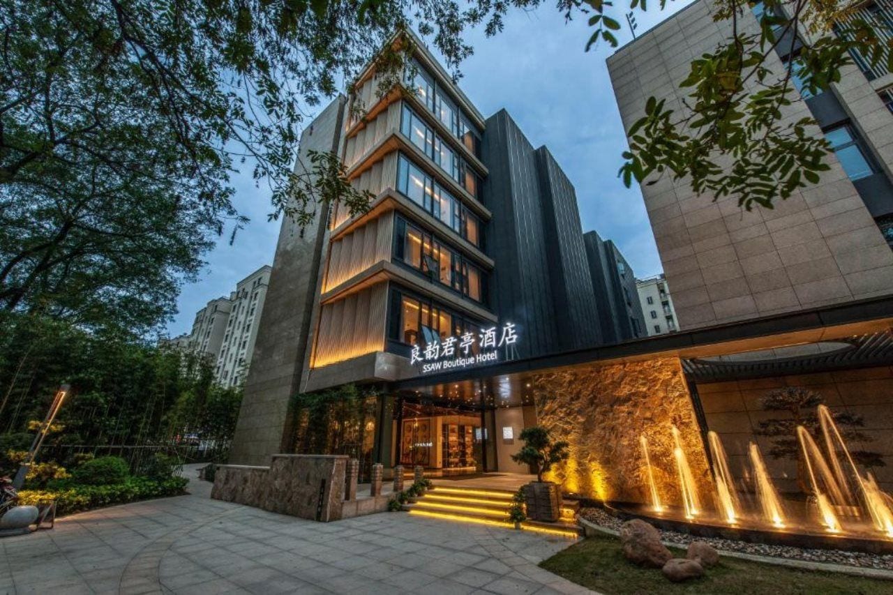 Un hôtel doté d’une façade moderne, d’une entrée bien visible et d’un espace paysager agrémenté d’un élément aquatique.