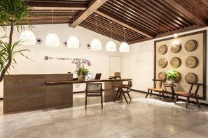 Un área de recepción con un mostrador de madera, varias sillas, lámparas colgantes y una pared decorada con platos.