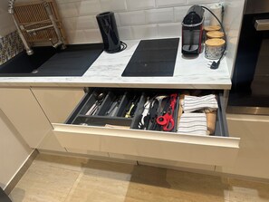 A kitchen counter with a coffee maker, a kettle, and a toaster. Below, a drawer contains various kitchen utensils.