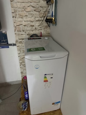 A white energy-efficient washing machine with a Candy Energy label, placed against a stone wall.