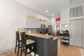 A kitchen with a central island, bar stools, and a microwave. - Bella Roja - Cozy St Augustine Home - Walkable (St. Augustine)