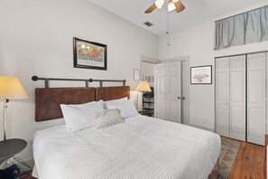 Ein aufgeräumtes Schlafzimmer mit Bett, Nachttischlampen, Deckenventilator und einem gerahmten Bild an der Wand.