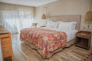 Un dormitorio con una cama grande, una mesita de noche de madera, una silla y un cabecero tejido.