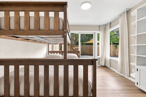 Ein Zimmer mit Etagenbett, großem Fenster mit Vorhängen und einer weißen Regaleinrichtung.