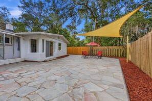 Eine Terrasse mit Steinboden, Holzzaun und einem gelben Sonnensegel.