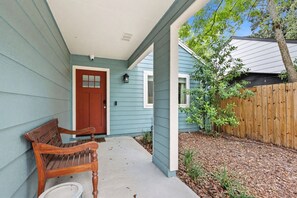 A porch with a wooden bench, a red door, and a small tree. - Near UF & Downtown | Spacious Home + Backyard (Gainesville)