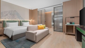 A hotel room with two beds, a sofa, a television, and a kitchenette.