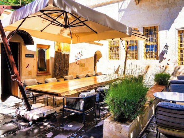 Een terras met een lange tafel en stoelen, een bord met daarop een receptie en een muur met een raam.