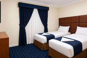 Ein Hotelzimmer mit zwei Betten, einem Holztisch und einem großen Fenster mit Vorhängen.
