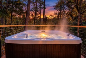 Een hottub omringd door een houten terras en bebossing.