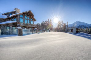 A snow-covered ski resort with a large lodge featuring multiple windows and a balcony. - Cozy Big Sky 5 bedroom home with private Lodge access, ski in/out, NEW RELEASE (Big Sky)