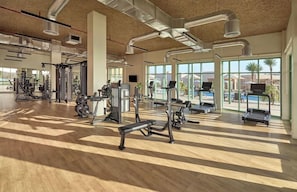 Une salle de sport équipée de divers appareils d’exercice, dotée de grandes fenêtres et d’un plancher en bois.