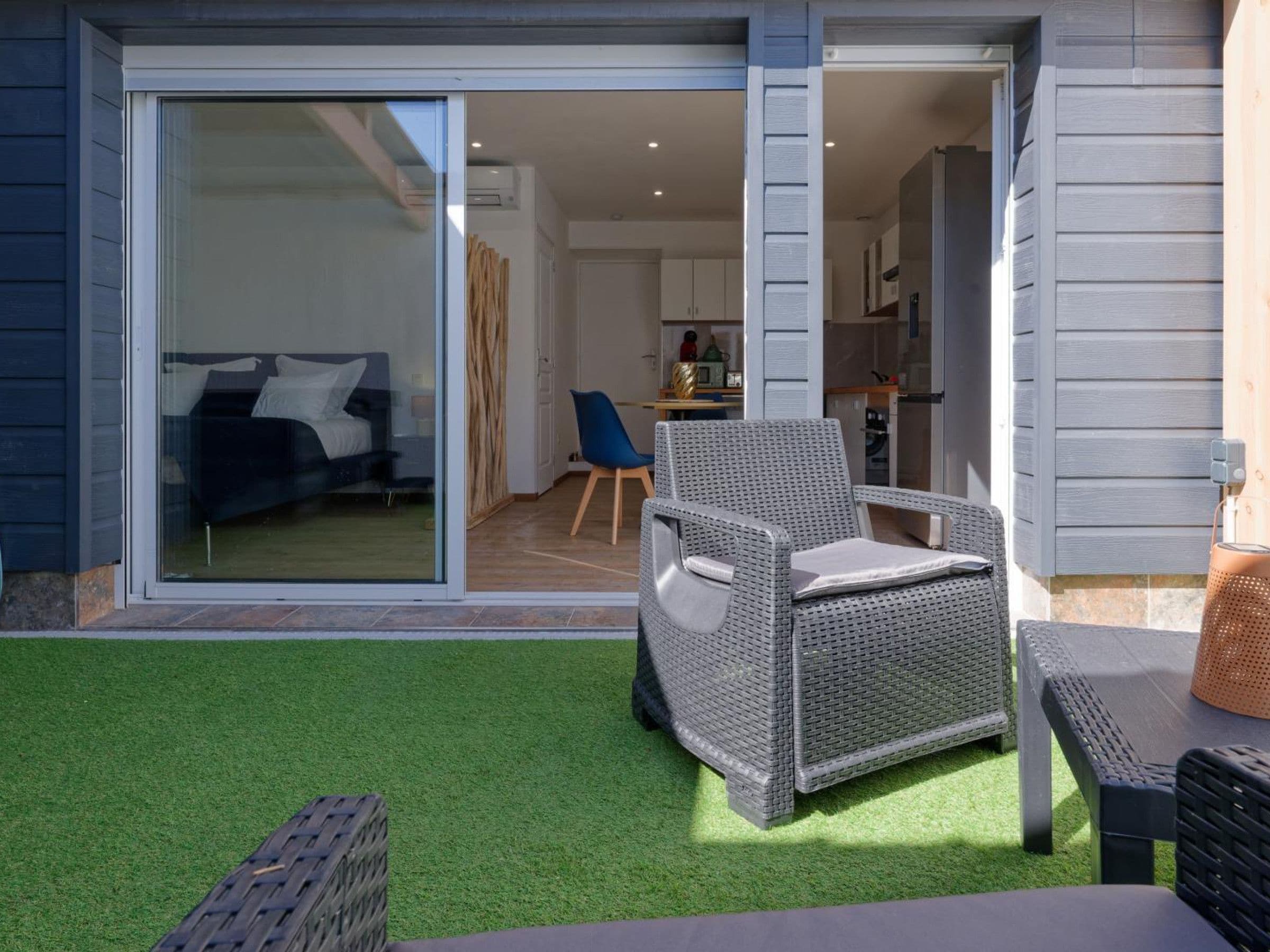 A modern outdoor living area with a patio, a dining set, and a sliding glass door leading to a bedroom.